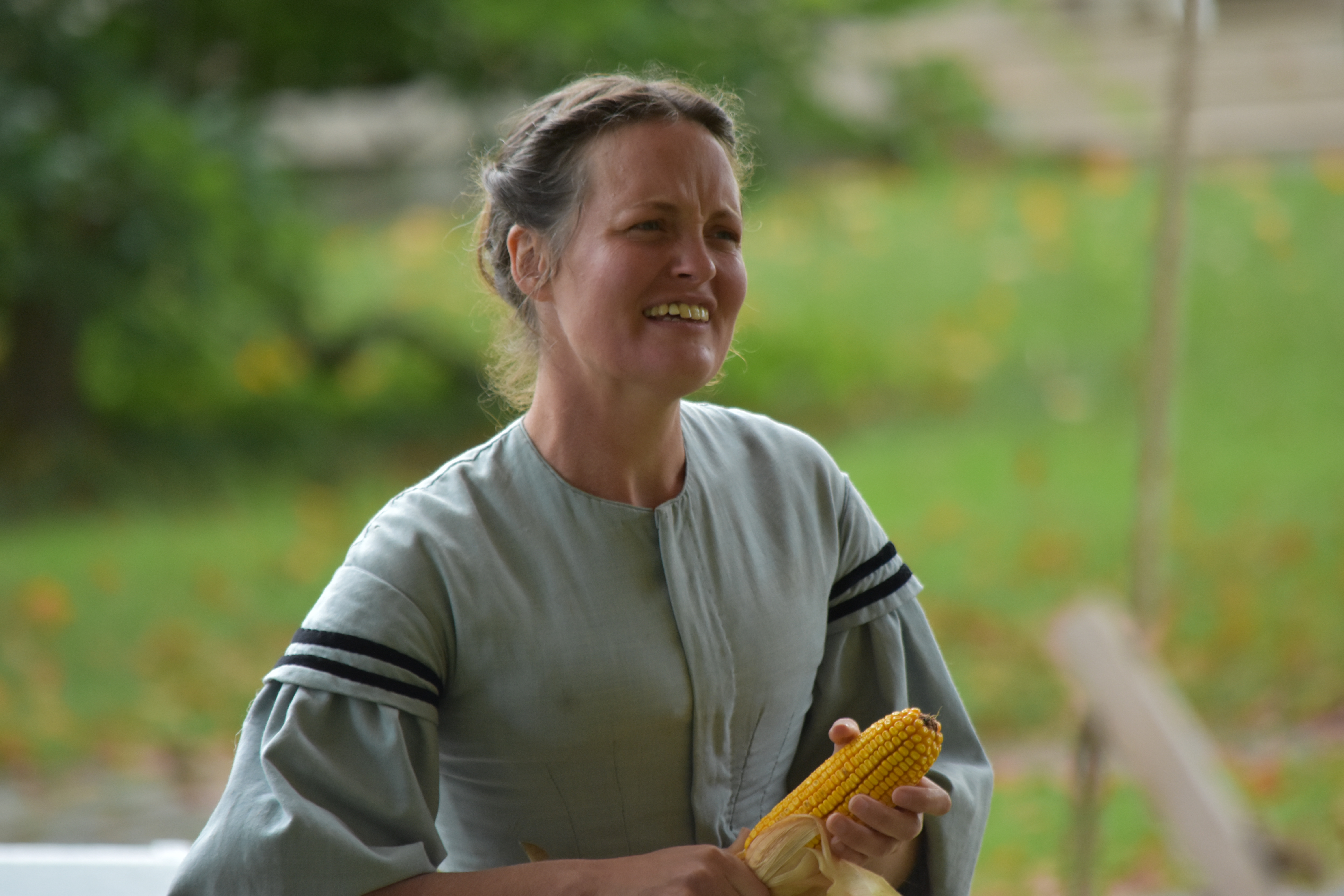 a woman in historic attire holding an ear of corn