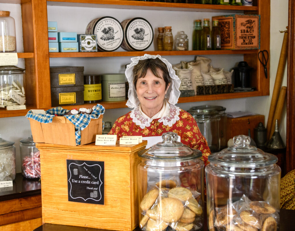 woman in historic attire standing behind a sales counter