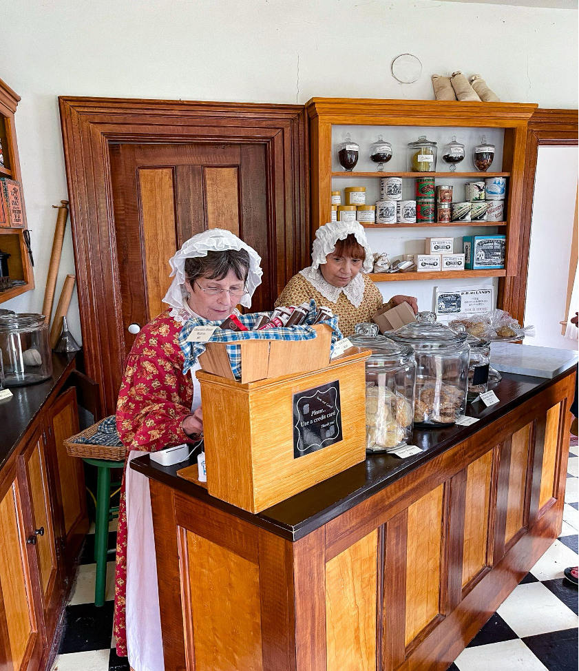 Two women in historic attire behind a grocery counter